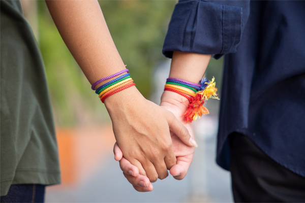 Hands of LGBTQIA+ women, holding together, rainbow bands around their wrists